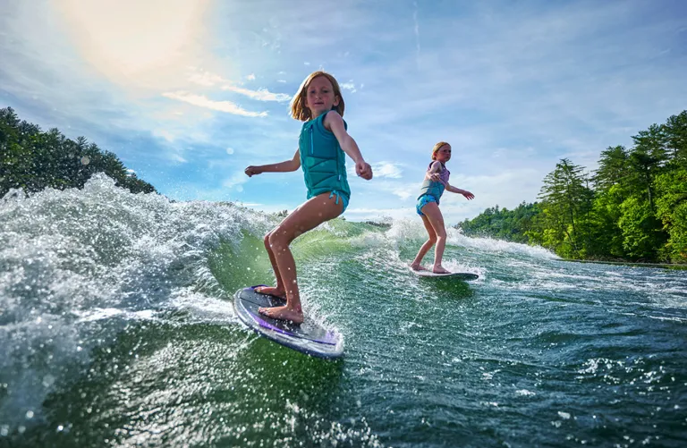 girls surf behind Axis boat