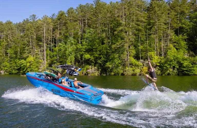 people surf behind Axis boat